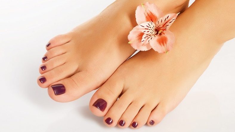 Schöne Füße mit dunkelrotem Nagellack, dekoriert mit einer zarten blühenden Blume.